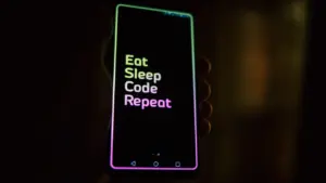 Dłoń trzymająca smartfon z podświetlonym ekranem w ciemnym, nocnym pomieszczeniu.