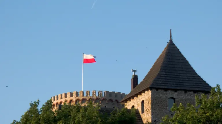 Zamek w Będzinie z powiewającą polską flagą na tle bezchmurnego, błękitnego nieba.