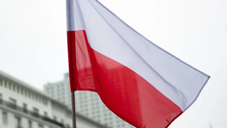 Polska flaga powiewająca na wietrze na tle historycznej miejskiej zabudowy.