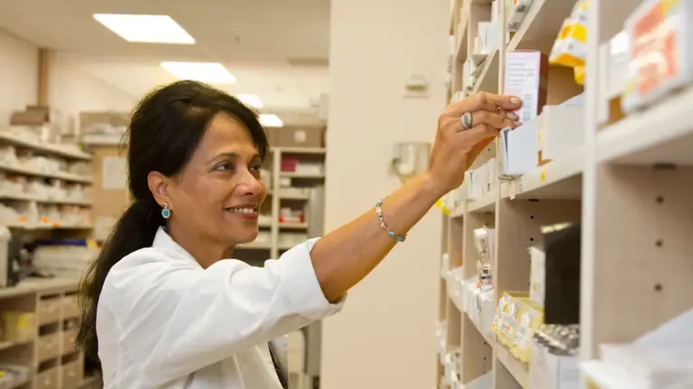 Farmaceutka sięgająca po opakowanie leku z półki w profesjonalnej aptece podczas codziennej pracy.